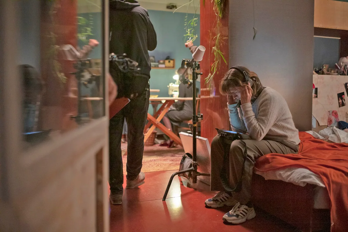 Dinnikova sitzt mit Kopfhörern und einem Bildschirm auf einem Bett.